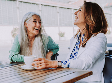Two women smiling and talking over coffee, representing comfortable patient experience and friendly dental care